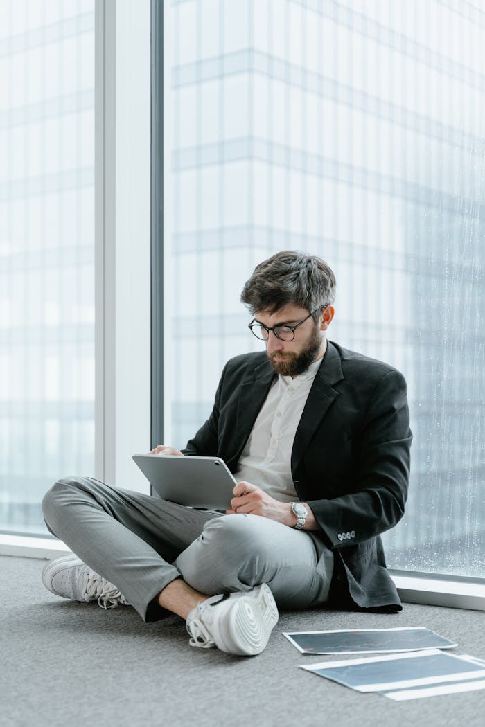 A man in a suit jacket analyzes a report on a tablet by a window.